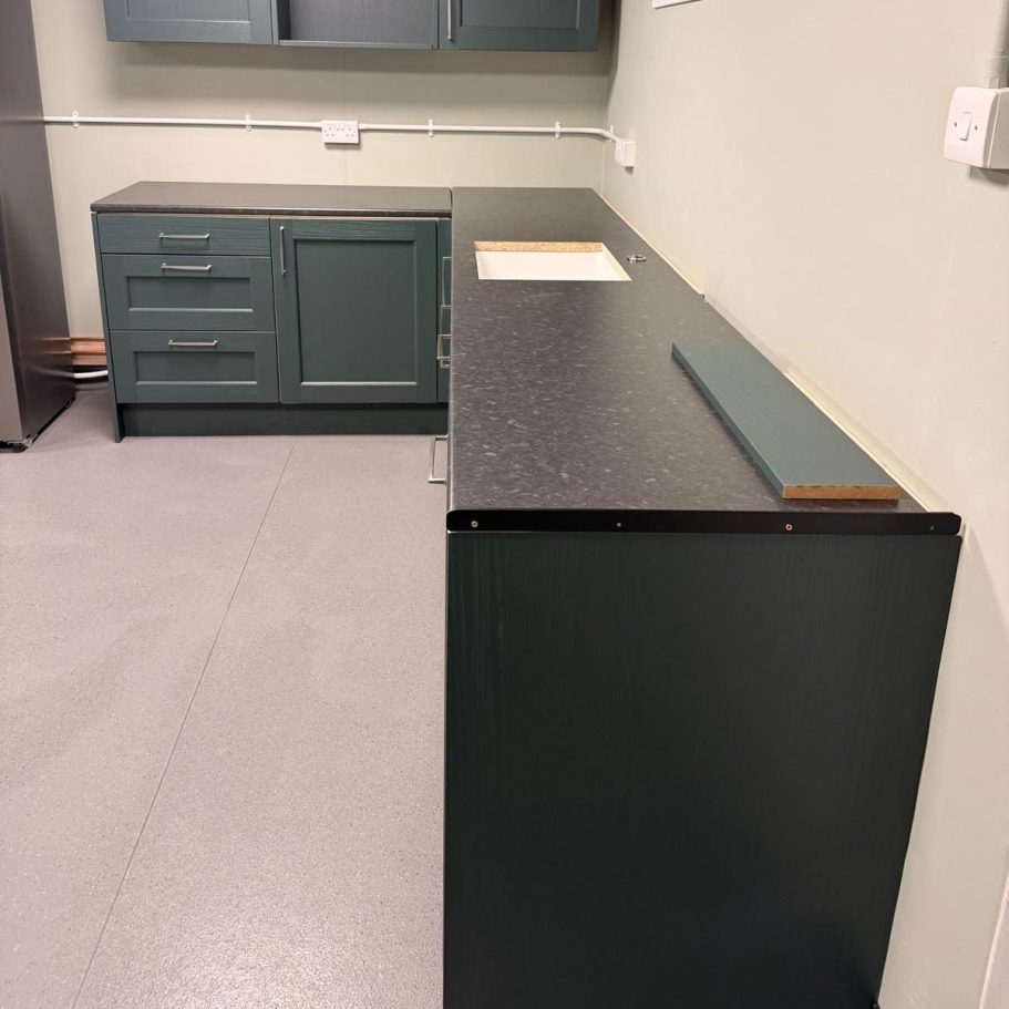 Commercial Deep Cleaning – After Photo | Professional Results/ clean sink & counter top Dark green kitchen cabinets and countertop in a well-lit room.