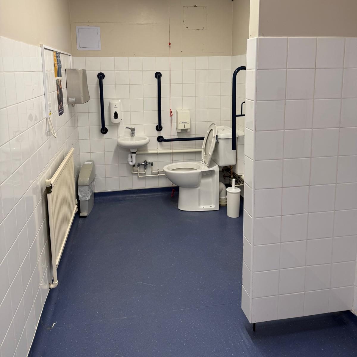 Commercial Deep Cleaning – After Photo | toilet Accessible restroom with white tiled walls and blue flooring, featuring a toilet and grab rails.