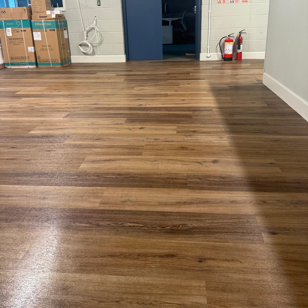 Commercial Deep Cleaning – After Photo | Floor cleaning A wooden floor in a room with boxes and a fire extinguisher visible.