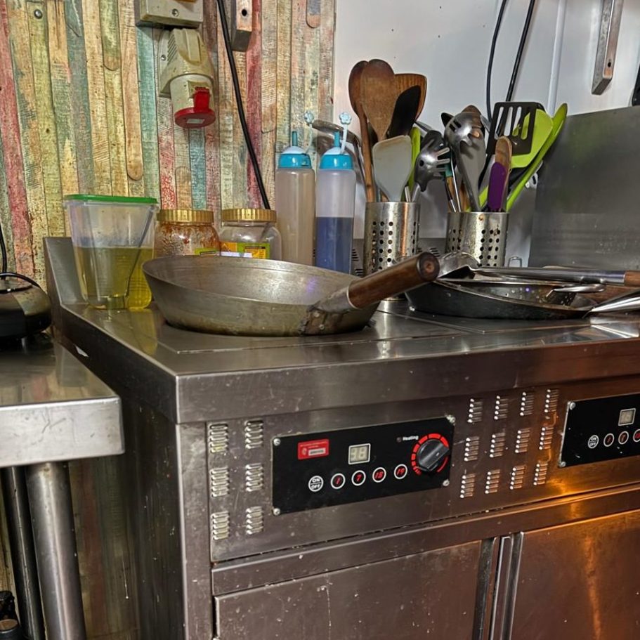 Commercial Cleaning – Restaurant | Before Photo A metal countertop with cooking utensils, jars, and a temperature control panel.