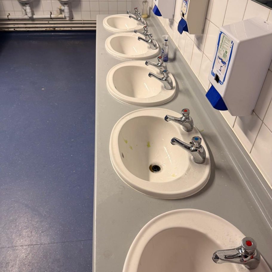 Commercial Deep Cleaning – Before Photo | Several sinks are dirty Row of five white sinks against a tiled wall in a bathroom.