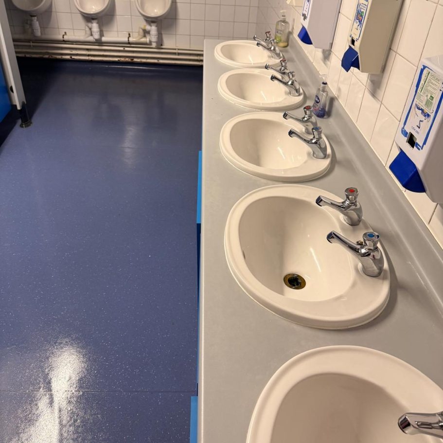 Commercial Deep Cleaning – After Photo | Several sinks are clean Row of white sinks with taps, blue flooring, and wall-mounted mirrors in a restroom.