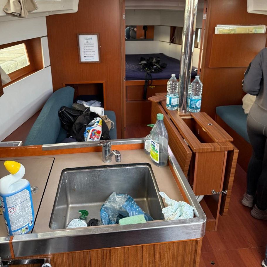 Marina Deep Cleaning – Before Photo | Professional Results/ Sink Interior of a yacht showing a sink, cleaning supplies, and a person in the background.