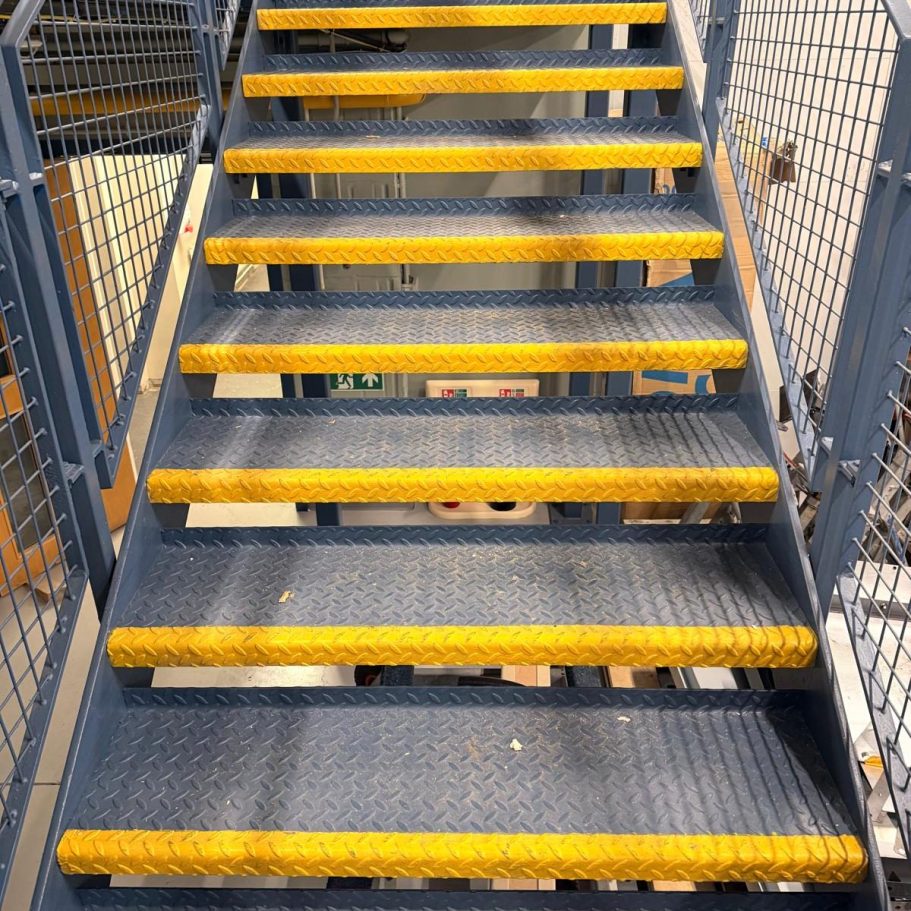 Commercial Deep Cleaning – Before Photo | Professional Results/ Stairs Steel stairs with yellow safety treads leading downward.
